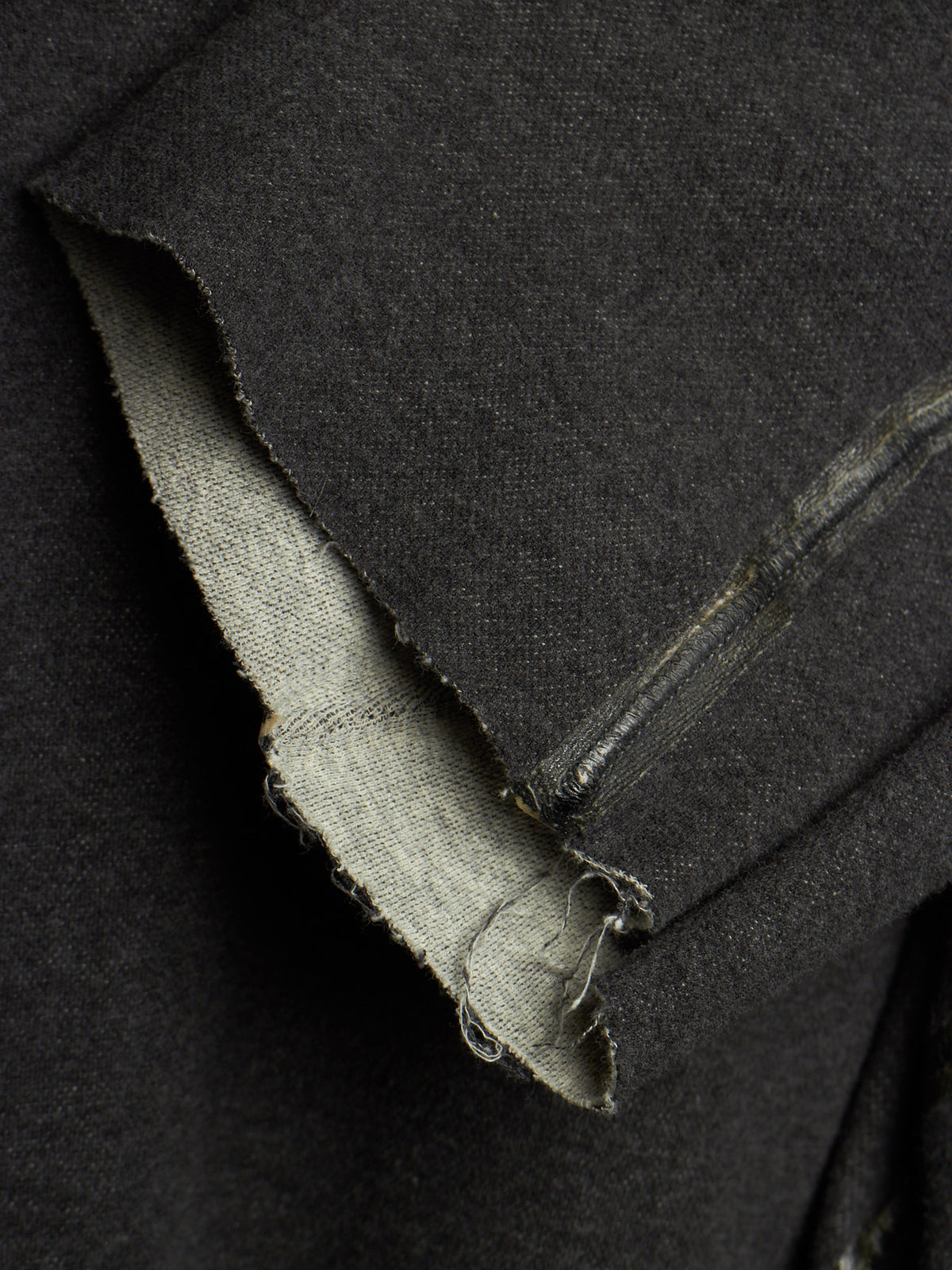 Close-up of a dark charcoal gray fabric garment, showing a raw, frayed hem and the lighter inner lining.