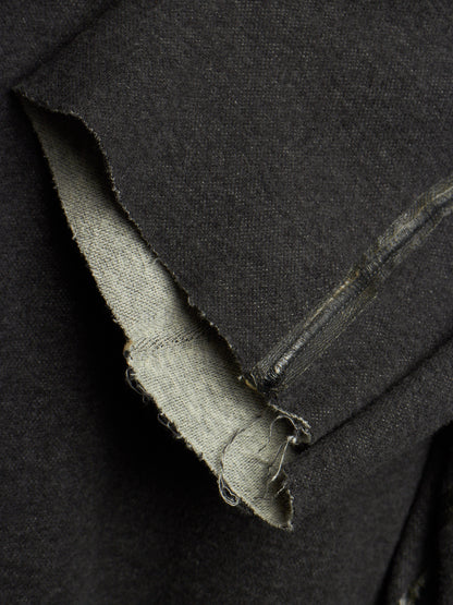Close-up of a dark charcoal gray fabric garment, showing a raw, frayed hem and the lighter inner lining.