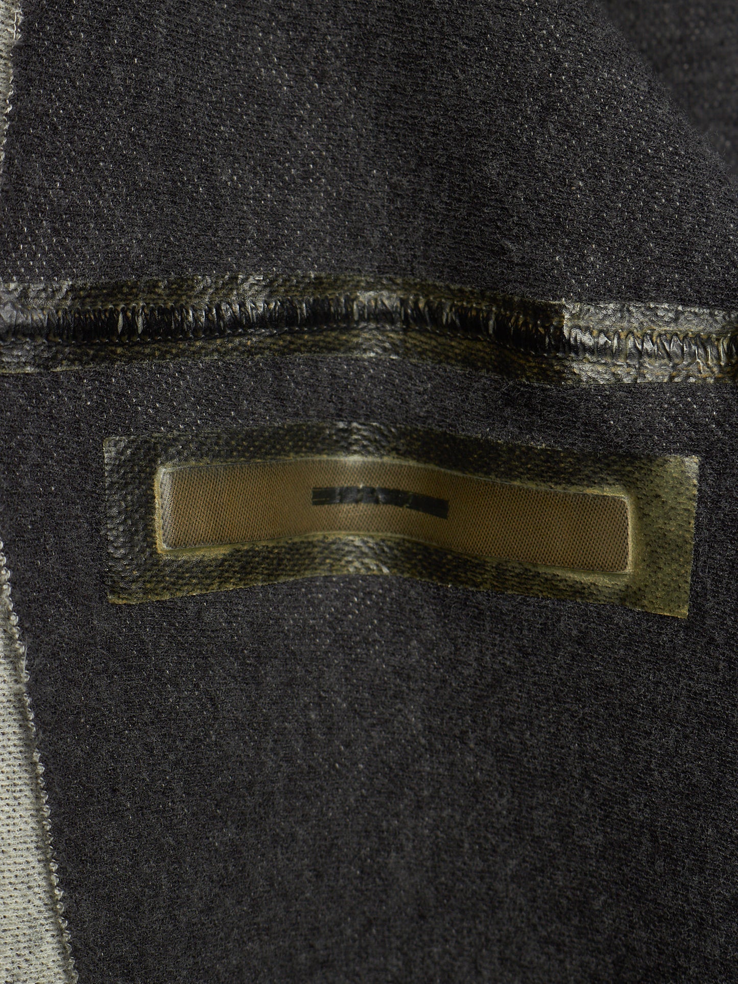 Close-up of a dark charcoal gray woven textile with a rectangular metallic gold label sewn onto the surface.