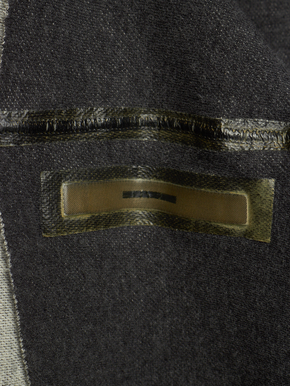 Close-up of a dark charcoal gray woven textile with a rectangular metallic gold label sewn onto the surface.