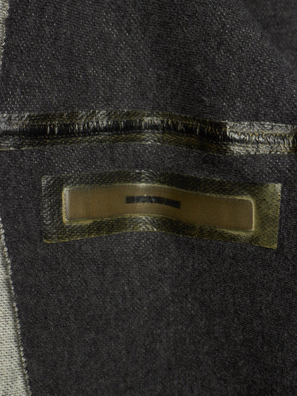 Close-up of a dark charcoal gray woven textile with a rectangular metallic gold label sewn onto the surface.