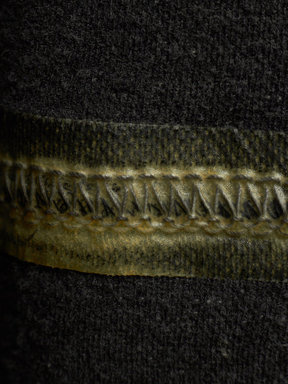 Close-up of a dark charcoal knit fabric with a horizontal band of metallic gold zipper teeth and dark gold stitching.