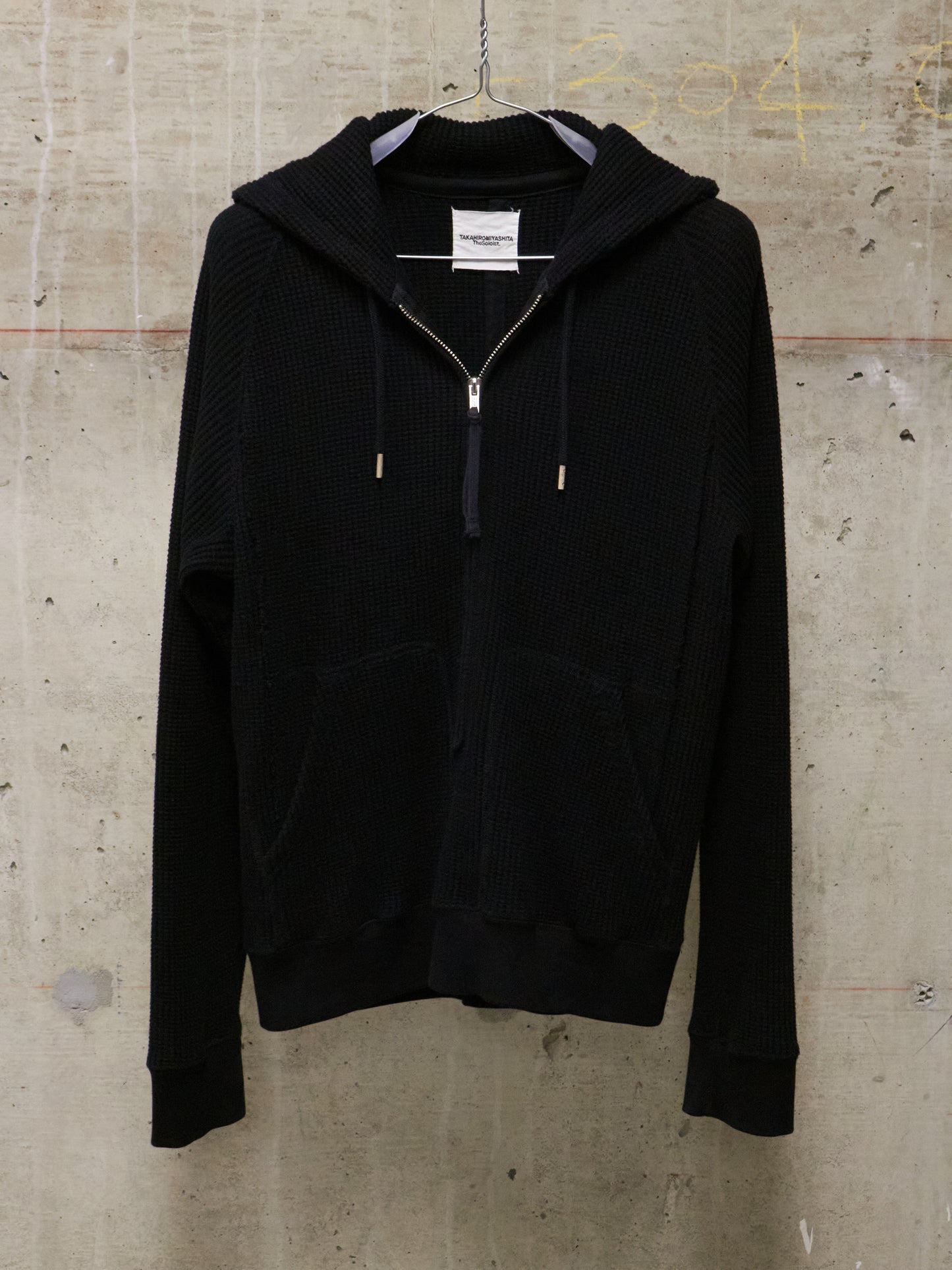 Black hoodie on a hanger against a textured beige wall