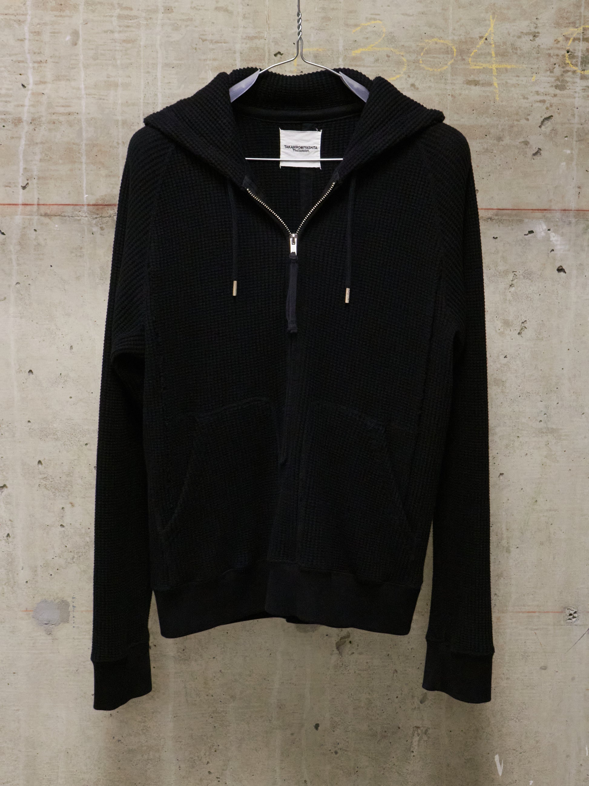 Black hoodie on a hanger against a textured beige wall