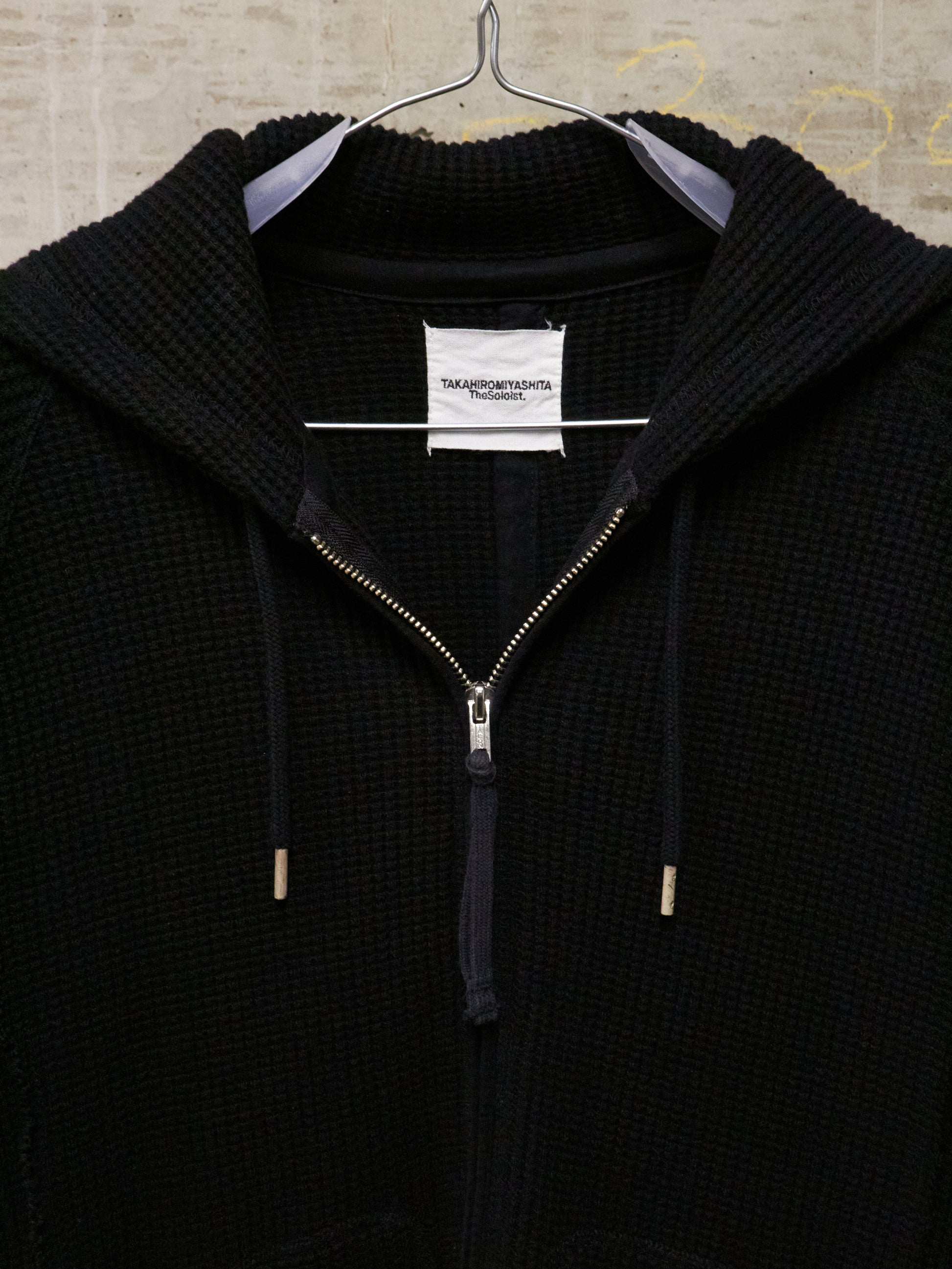 Black zip-up hoodie on a hanger with a visible brand label.