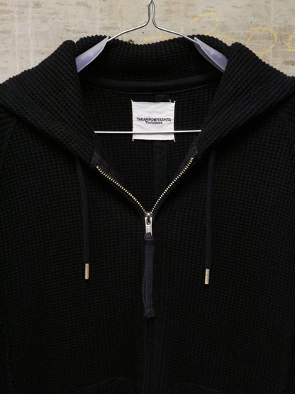 Black zip-up hoodie on a hanger with a visible brand label.