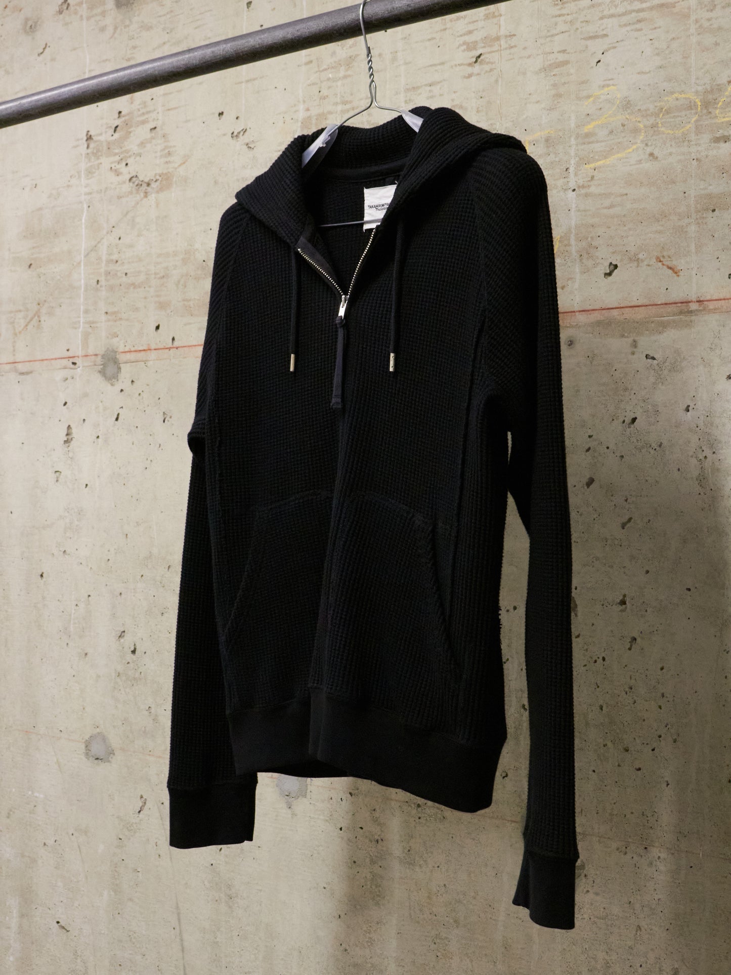 Black hoodie hanging on a hook against a textured wall.
