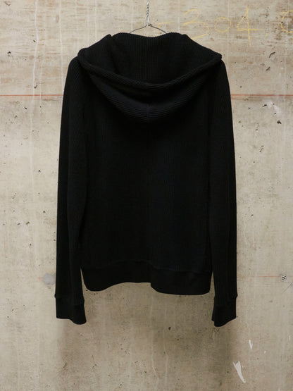 Black hoodie on a hanger against a textured wall.