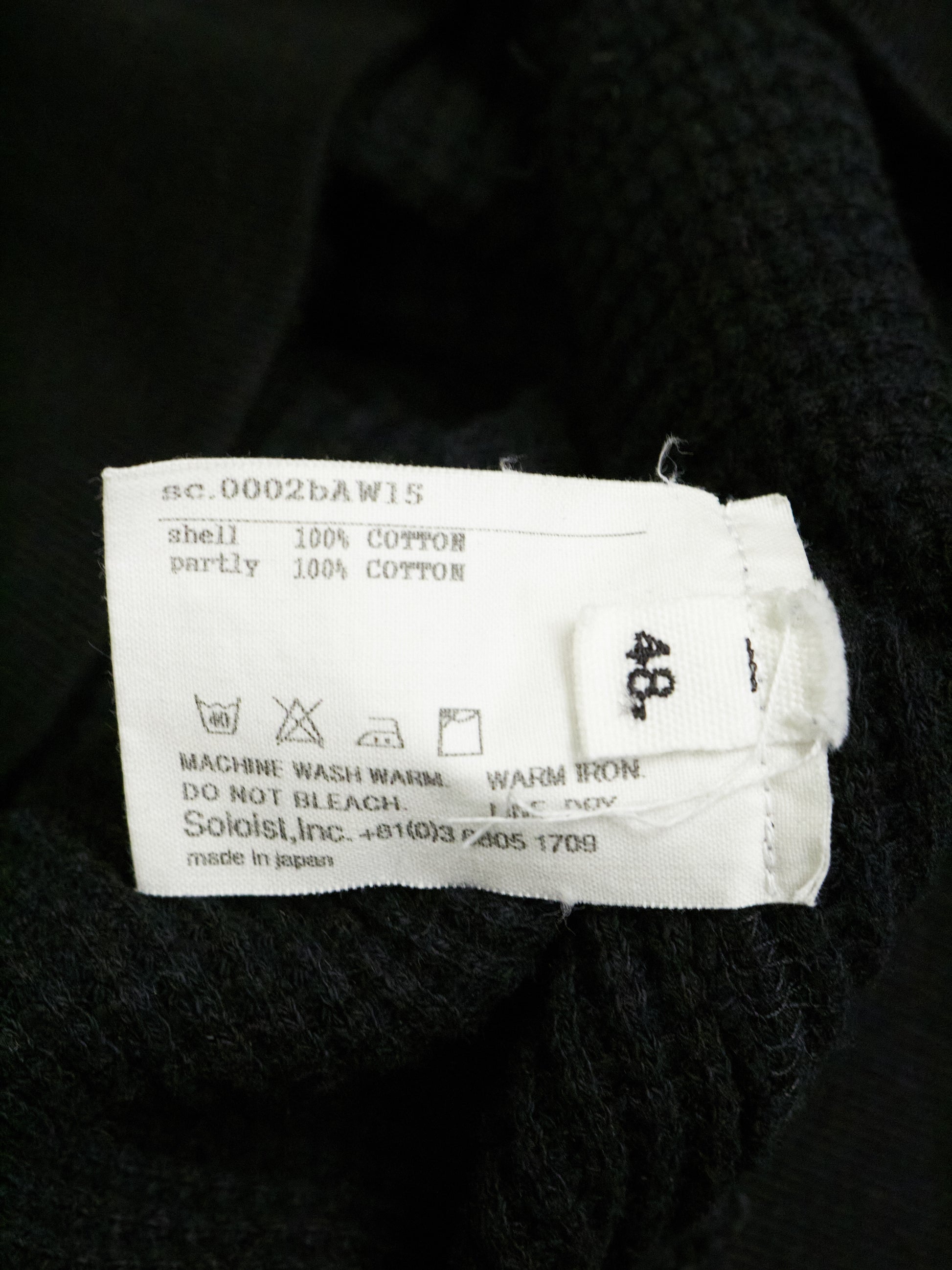 Clothing label on a black garment with text and symbols.