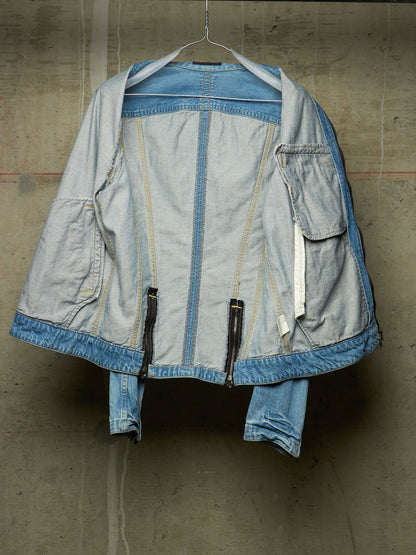 A light blue denim jacket with contrasting medium blue denim trim, hanging on a wire hanger against a textured concrete wall.
