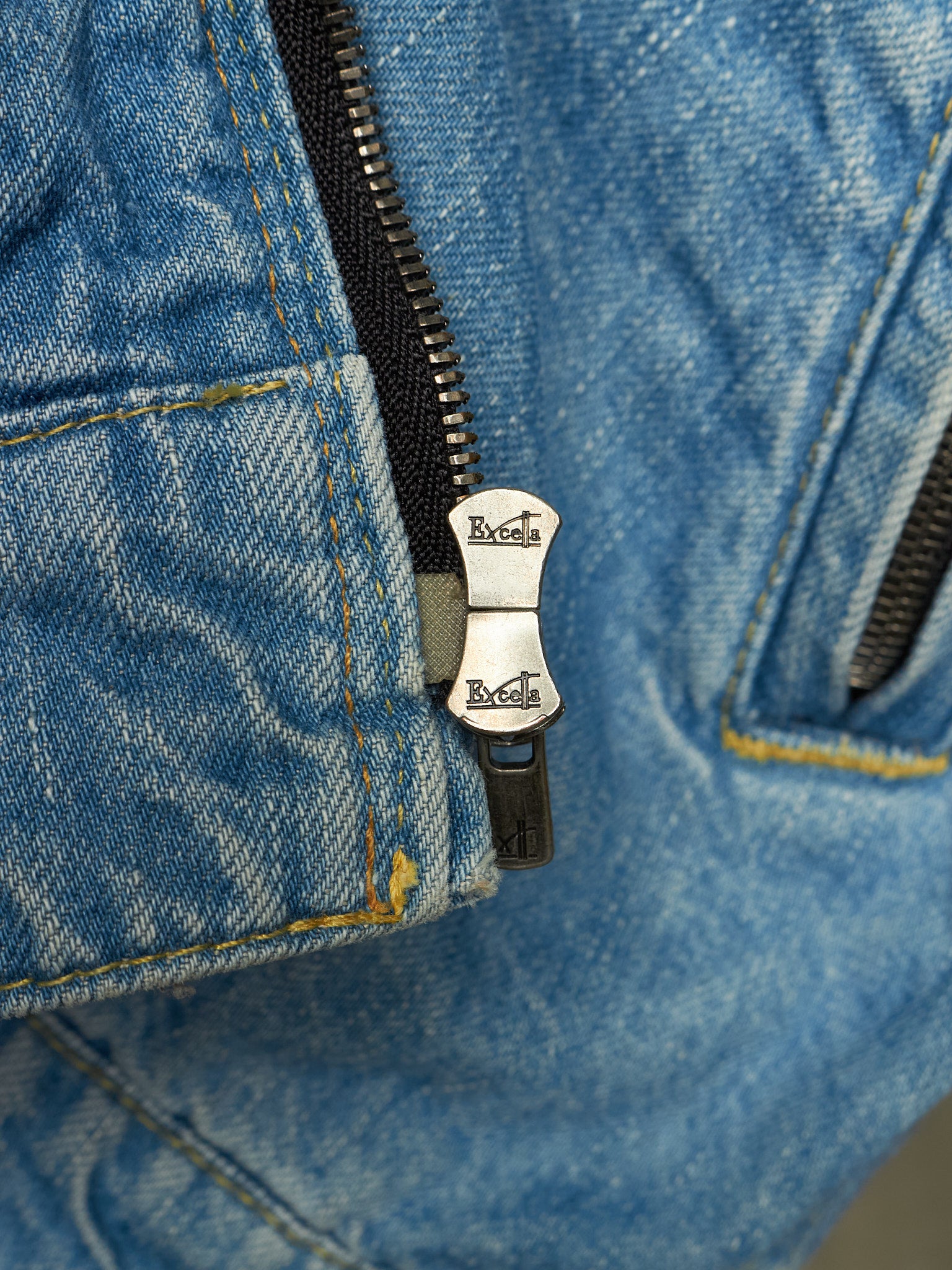 Close-up of a blue denim jacket with a black zipper and a silver metal pull tab engraved with the brand name 'Rexona'.