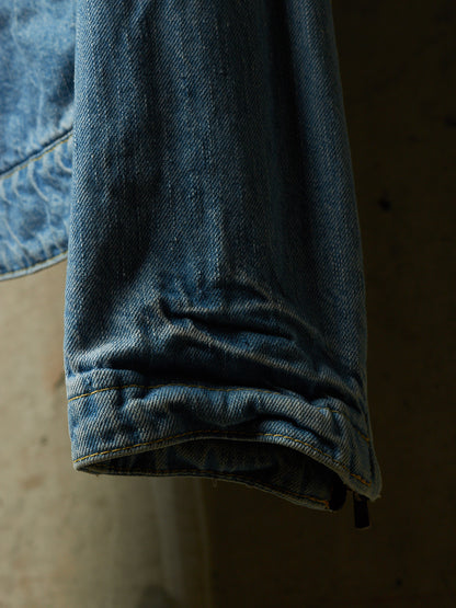 A close-up detail shot of a blue denim garment, showing the folded cuff and texture of the fabric against a dark, neutral background.