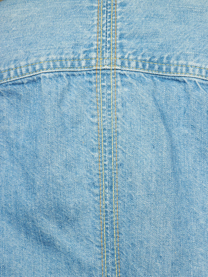 A close-up of light blue denim fabric showing the texture of the weave and a central double-stitched seam.