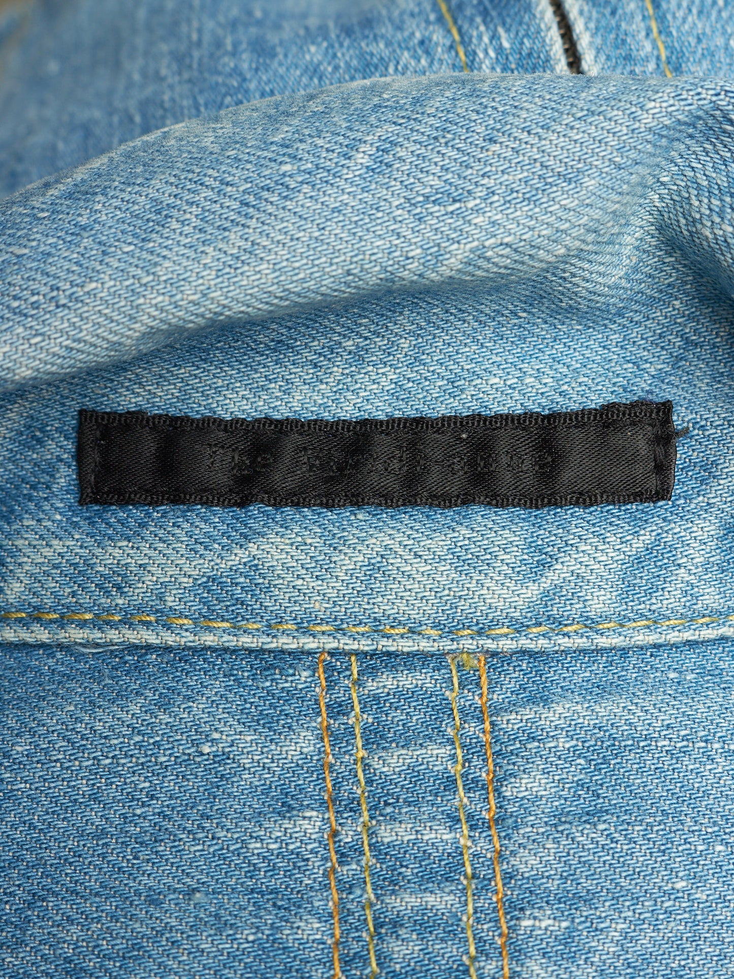 Close-up of a light blue denim fabric with a black rectangular sewn label stitched horizontally across the middle.