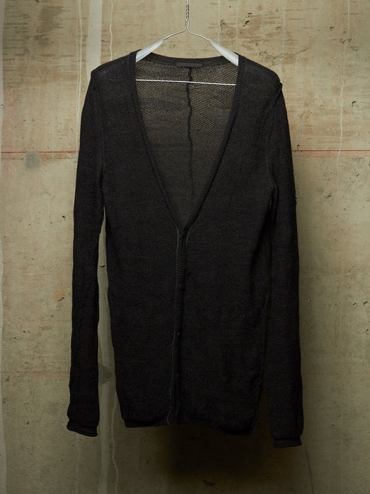 A black open-front cardigan sweater with a deep V-neck and long sleeves, hanging on a white plastic hanger against a textured concrete wall.