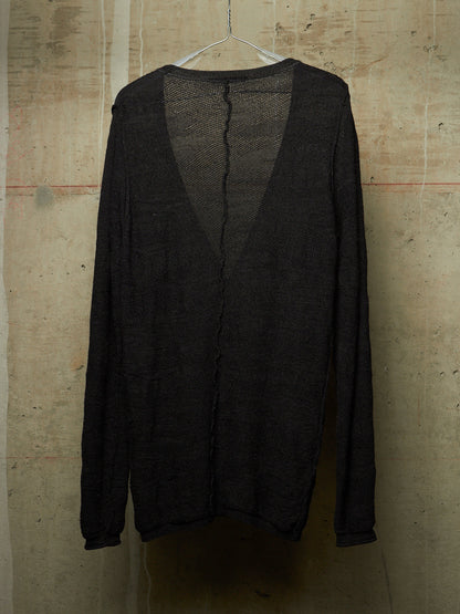 A black open-knit long-sleeve cardigan hanging on a white plastic hanger against a textured concrete wall.