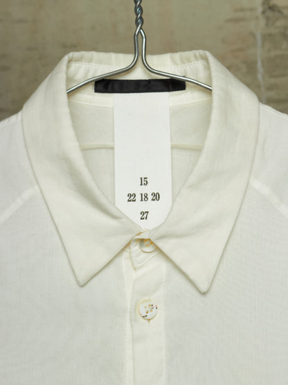 Close-up of a cream-colored knit collared shirt hanging on a metal hanger, with a white size tag sewn into the collar showing the numbers 15, 22 18 20, and 27.