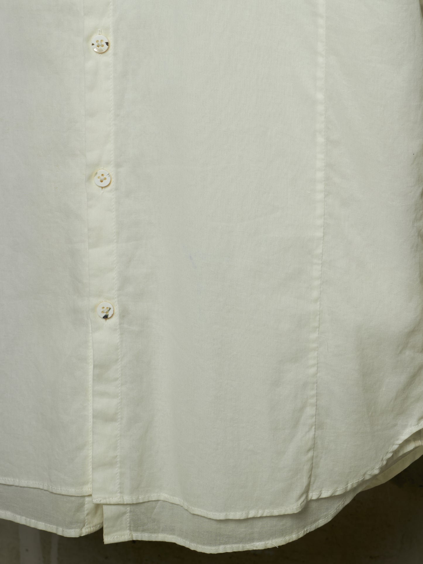 Close-up of a light cream or off-white button-up shirt fabric, showing the texture, stitching, and buttons.