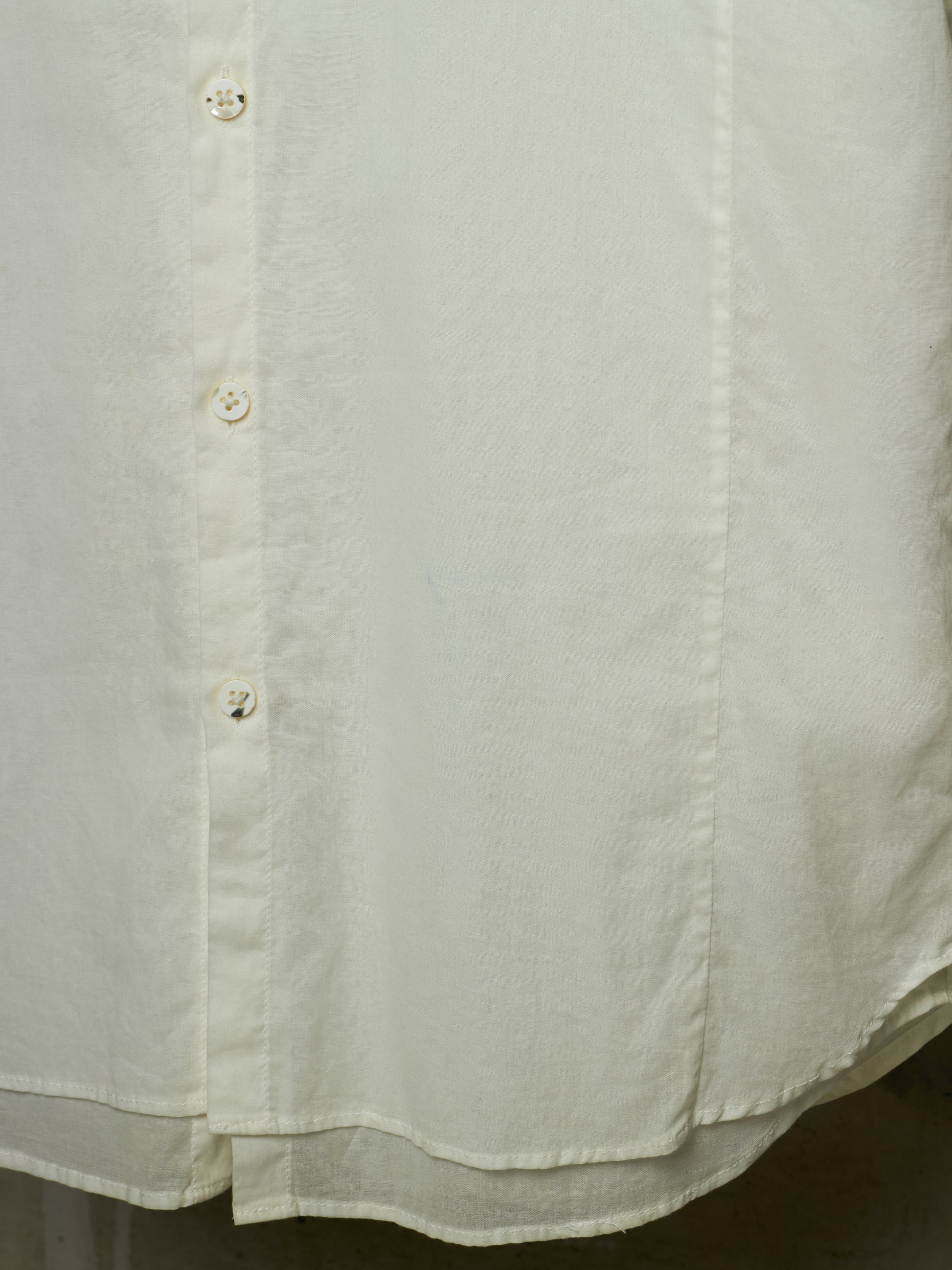 Close-up of a light cream or off-white button-up shirt fabric, showing the texture, stitching, and buttons.
