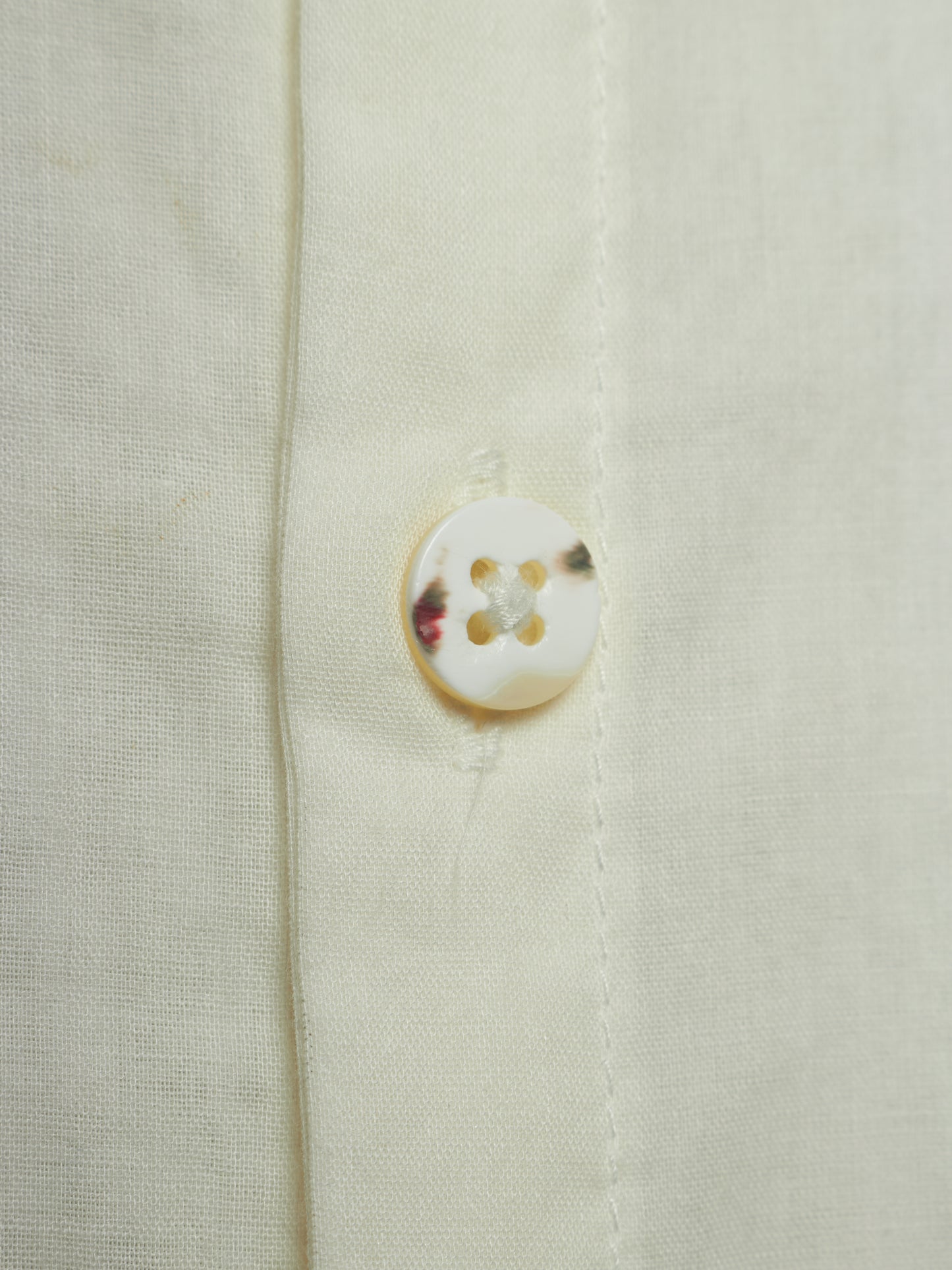 Close-up of a cream-colored linen shirt showing the fabric texture and a single round shell button.