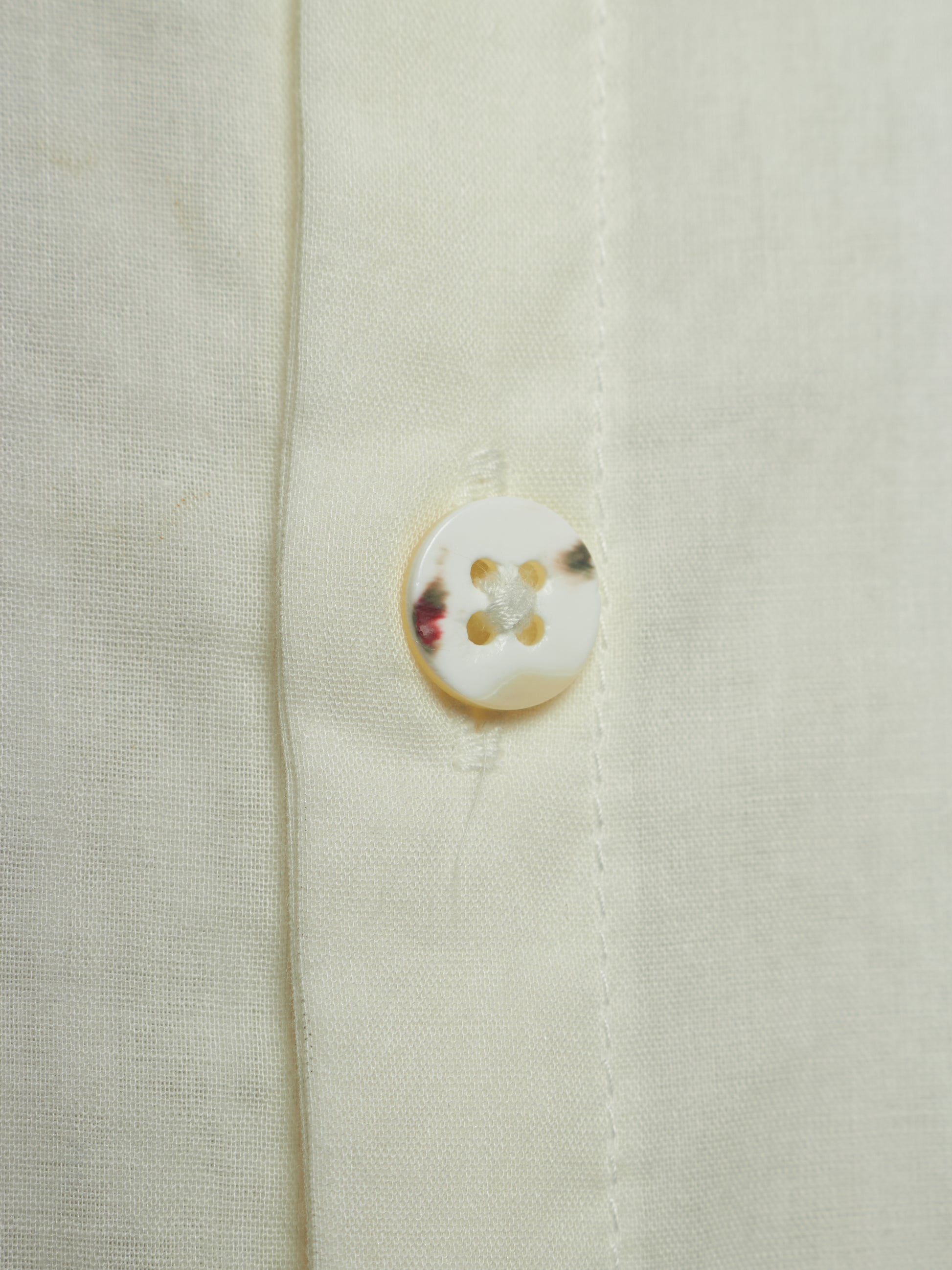 Close-up of a cream-colored linen shirt showing the fabric texture and a single round shell button.