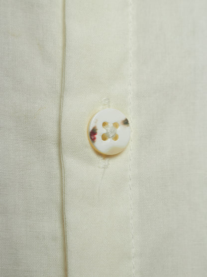 Close-up of a cream-colored linen shirt showing the fabric texture and a single round shell button.