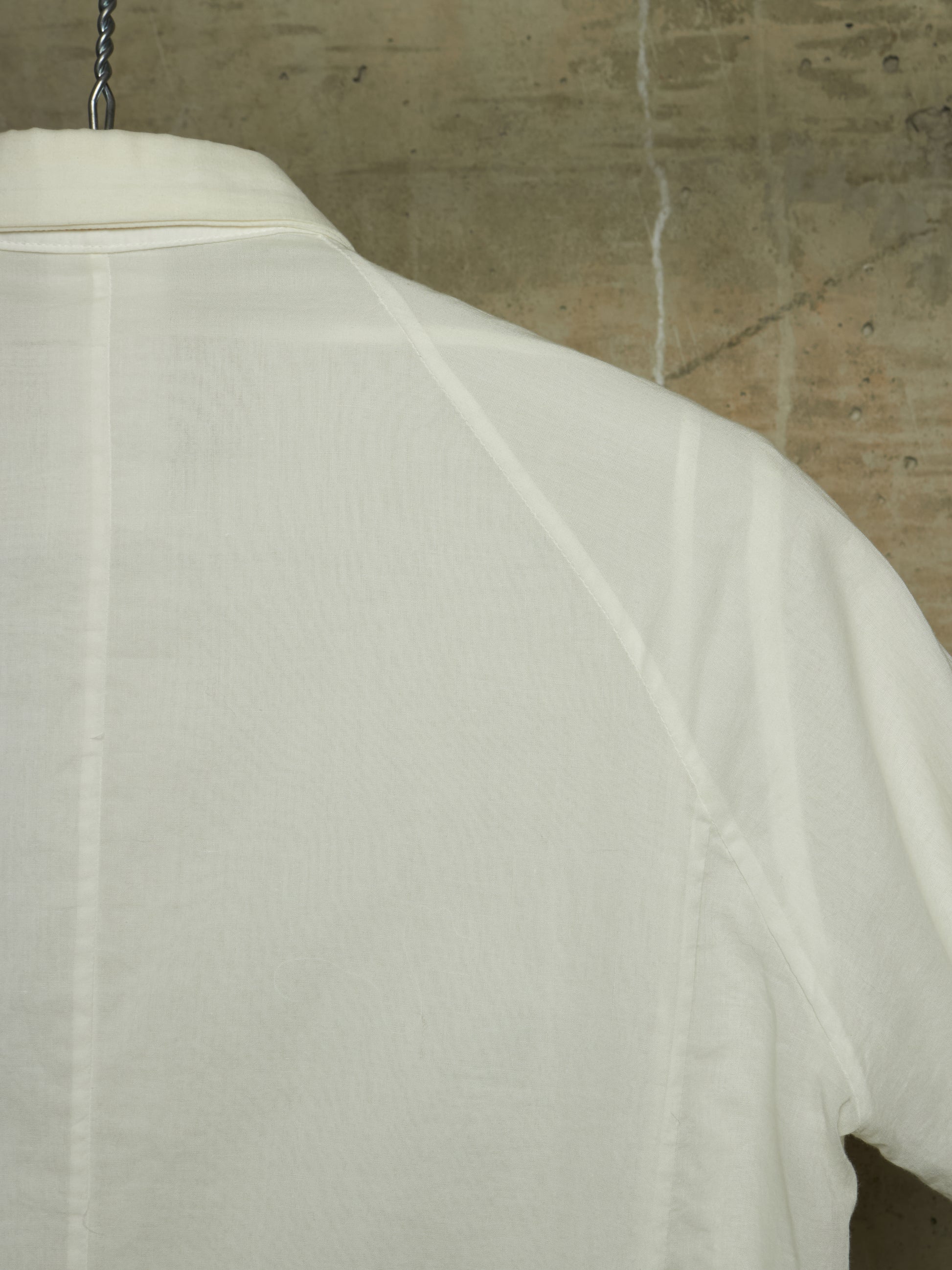 Close-up of the back of a white short-sleeve shirt hanging against a textured concrete wall.