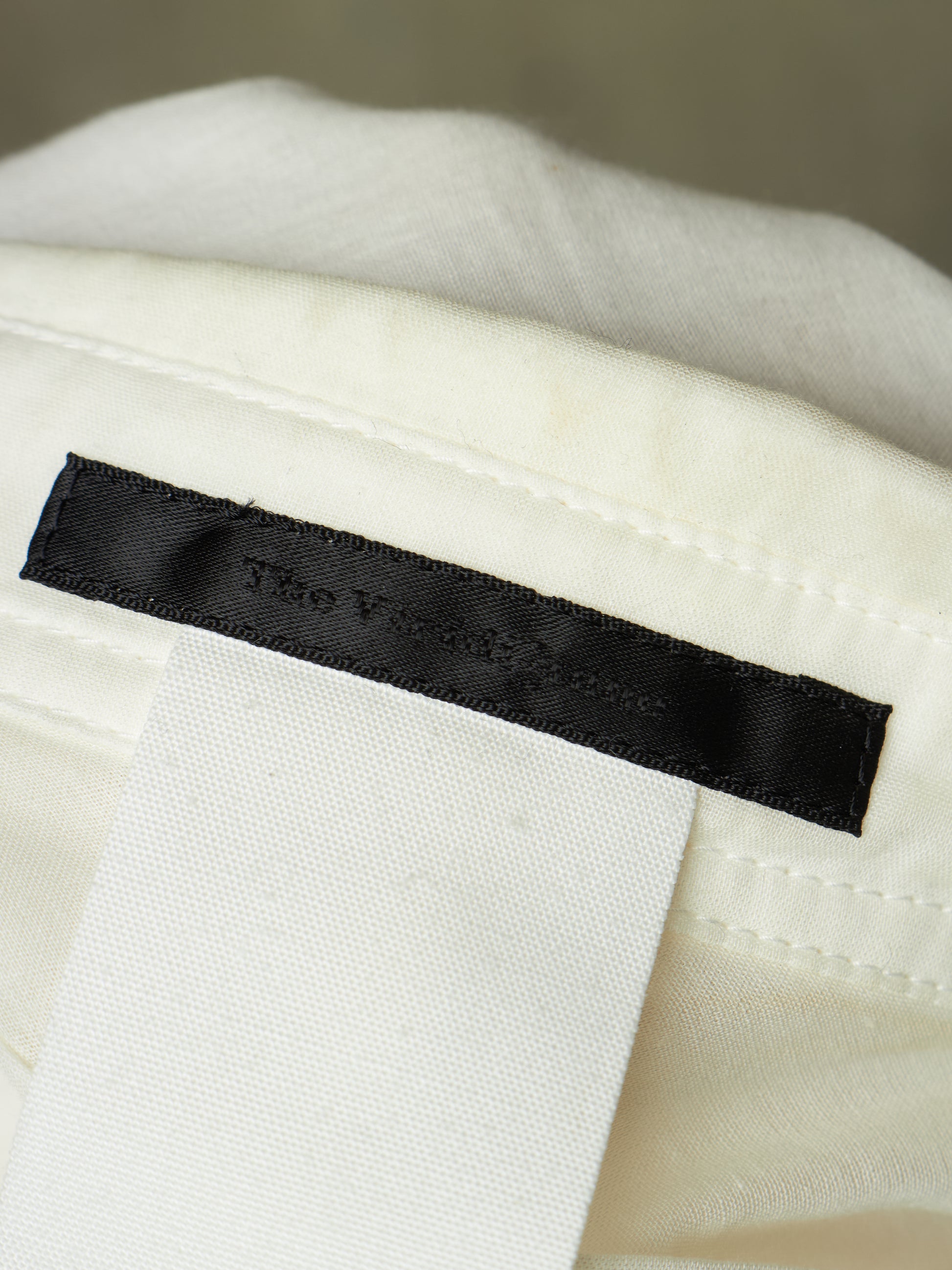 Close-up of a black fabric brand label sewn onto an off-white textile, with the embroidered text 'The Victoria House' visible.