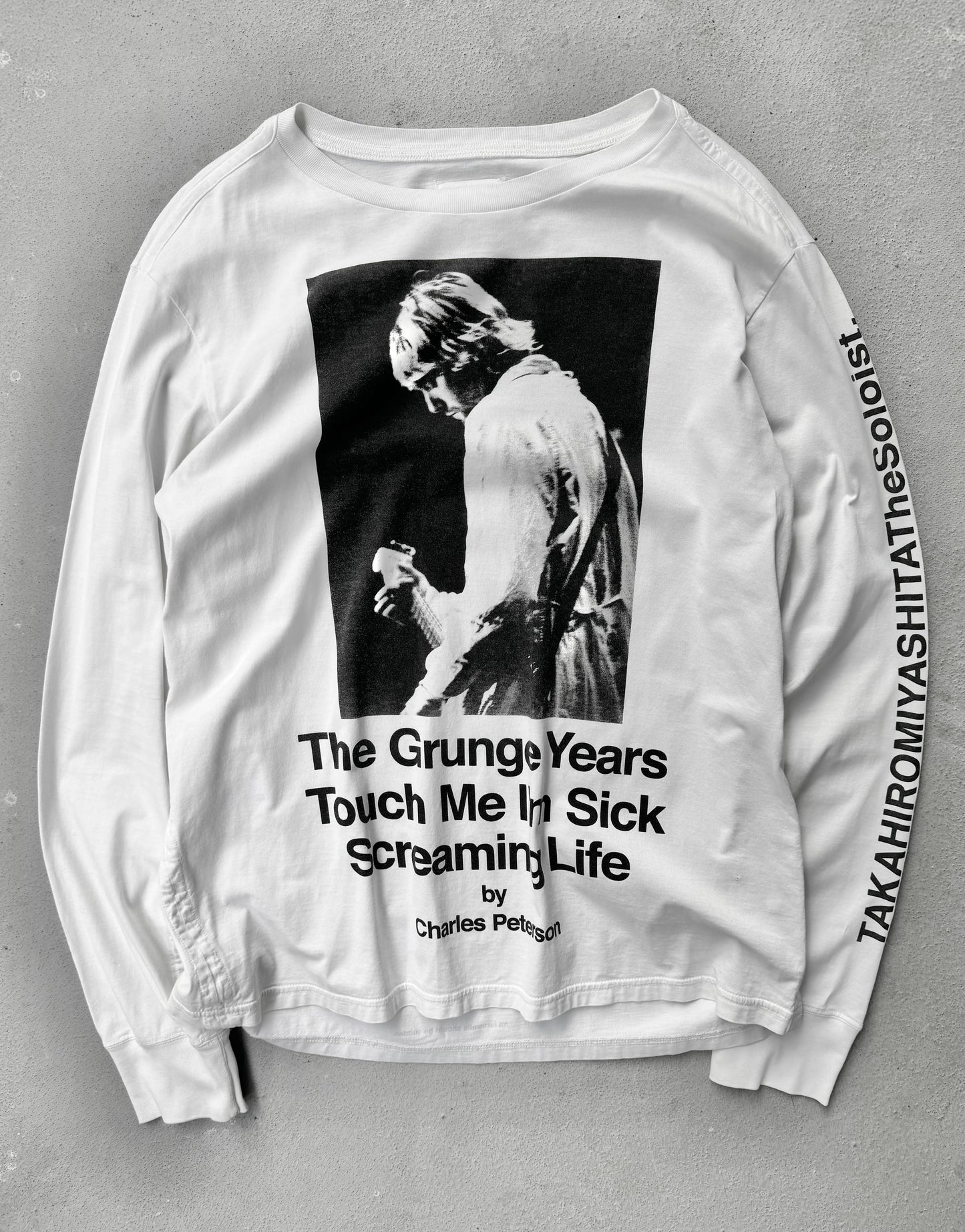 White long-sleeve shirt with graphic design and text on a gray background