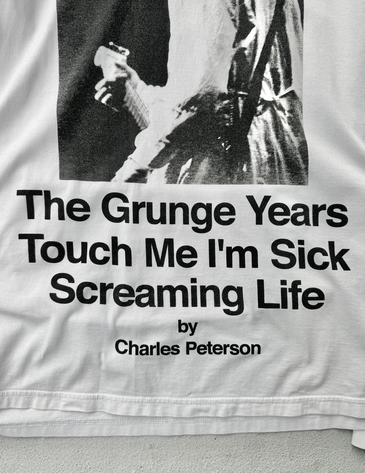 Text on a garment with a black and white photo of a person, featuring the quote 'The Grunge Years Touch Me I'm Sick Screaming Life' by Charles Peterson.