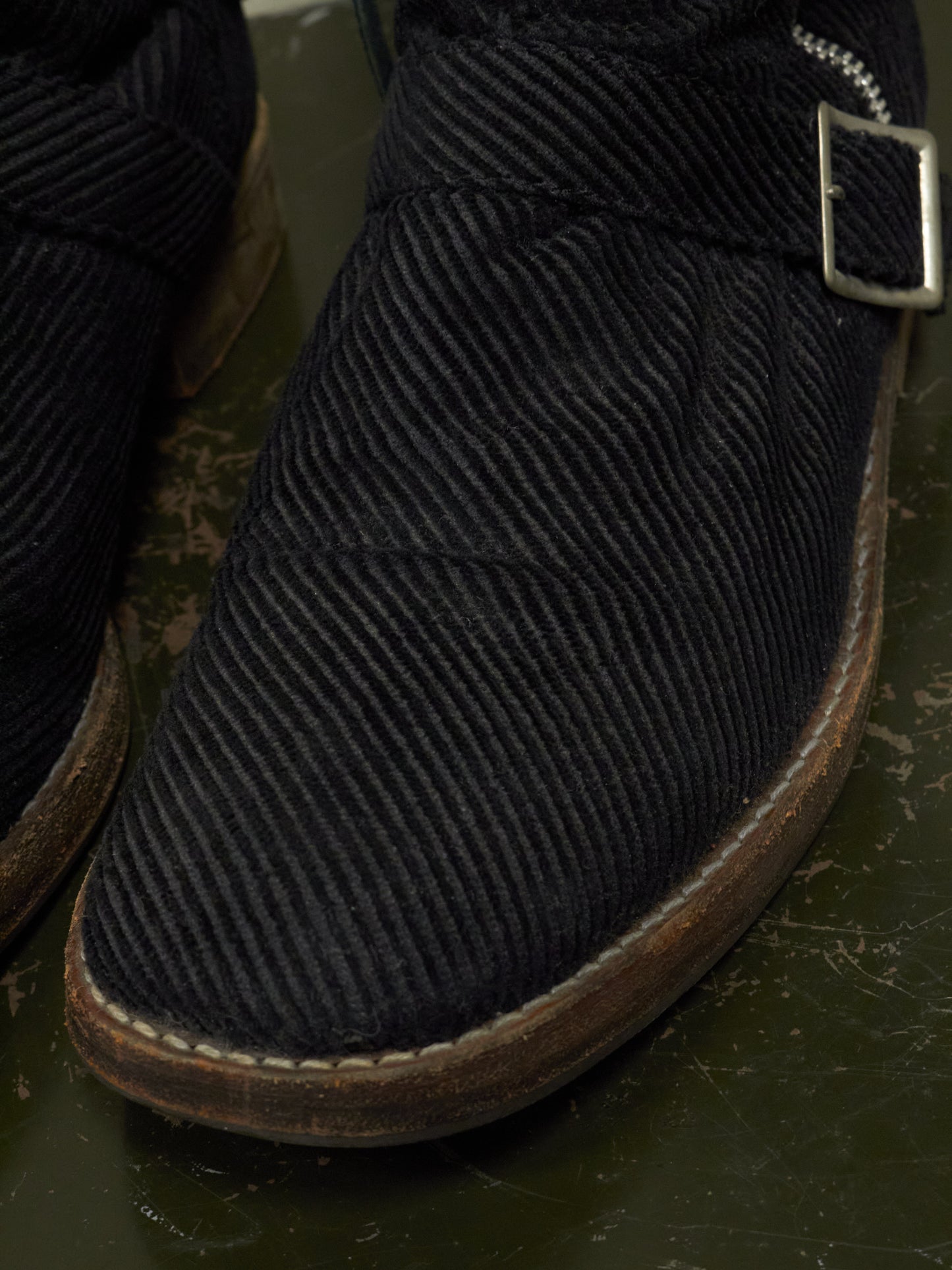 Close-up of a black corduroy boot with a buckle on a dark surface