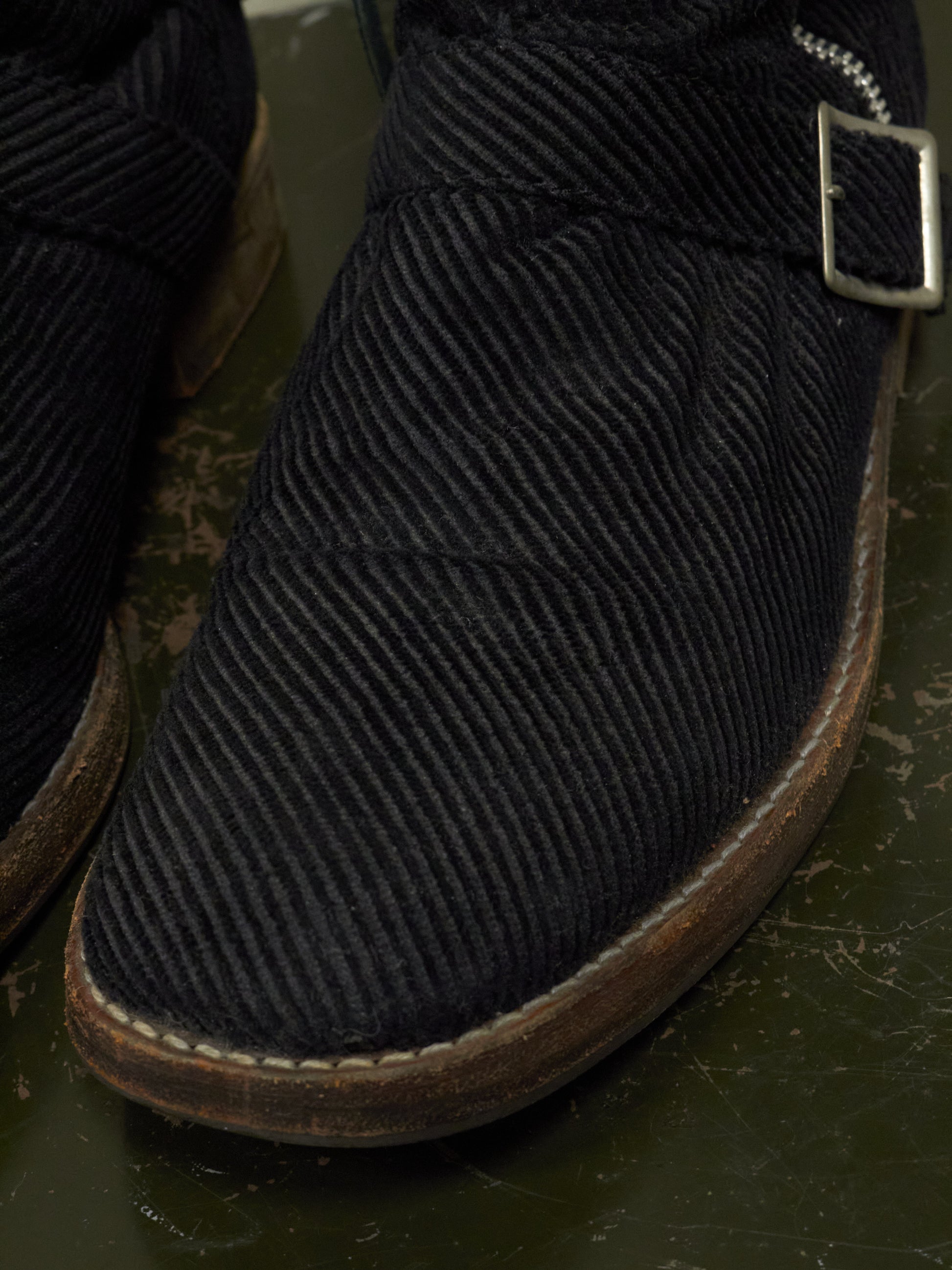 Close-up of a black corduroy boot with a buckle on a dark surface