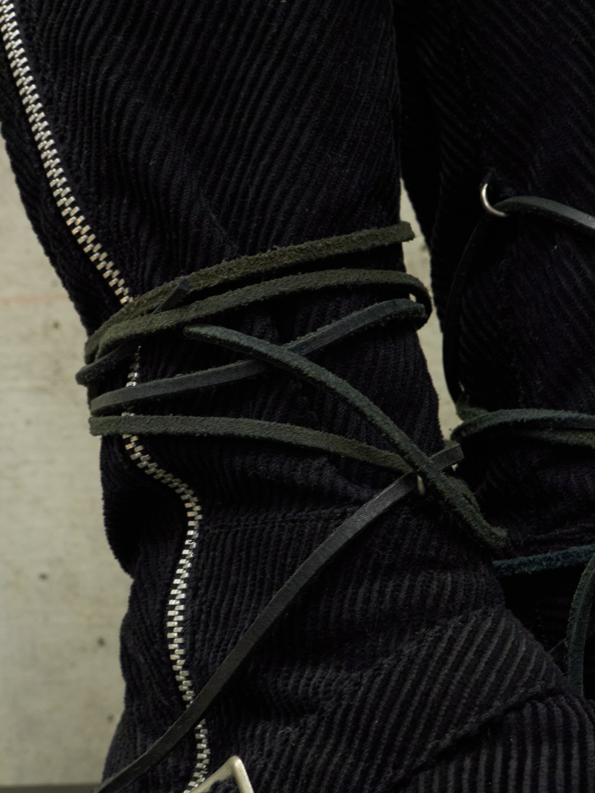 Close-up of a black corduroy jacket with green laces and zippers.