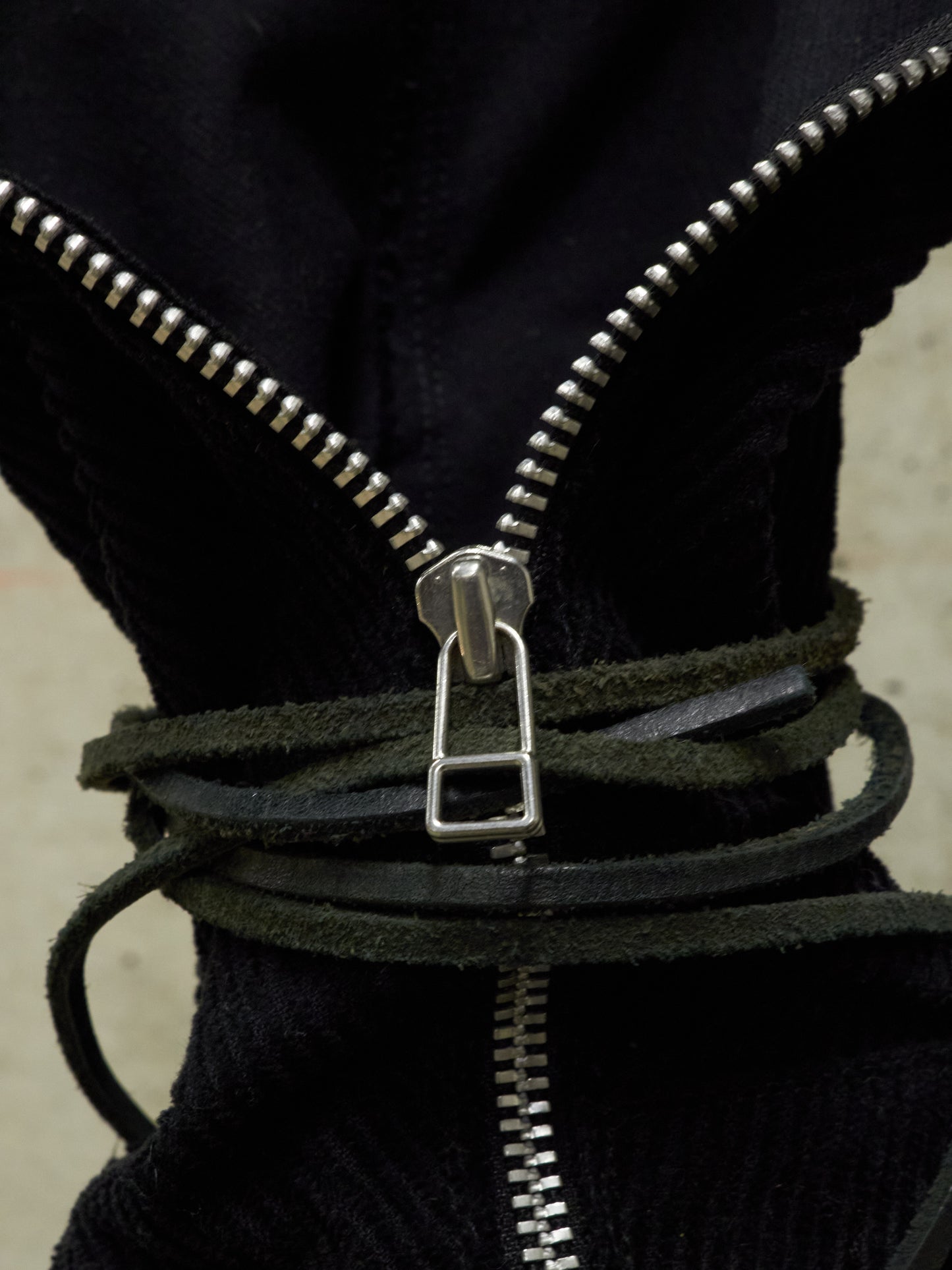 Close-up of a black jacket with a silver zipper and leather strap.