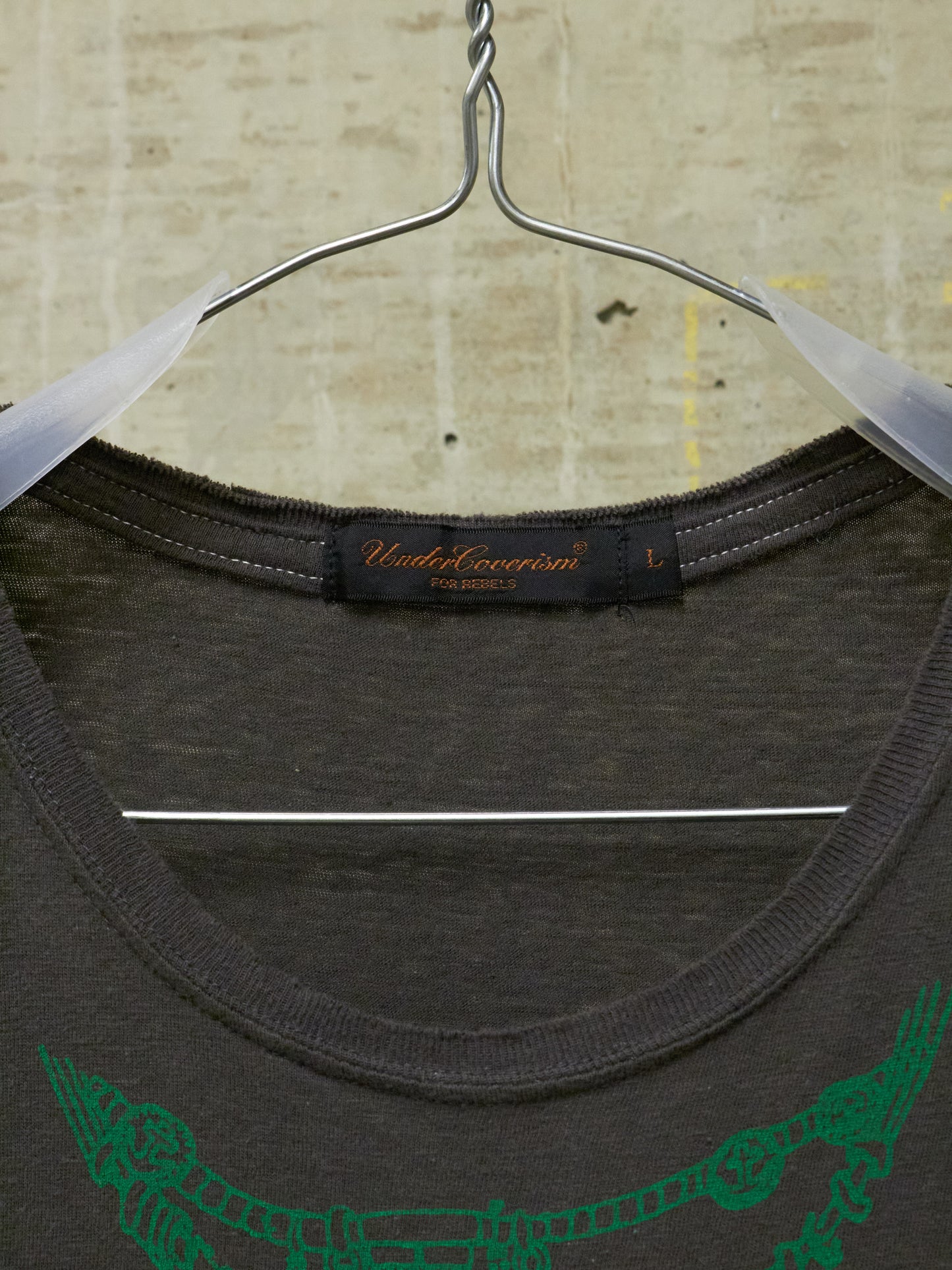 Dark gray t-shirt with green graphic design on a hanger against a textured beige background