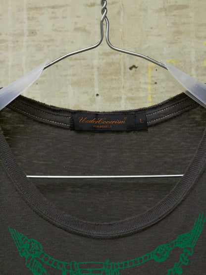 Dark gray t-shirt with green graphic design on a hanger against a textured beige background