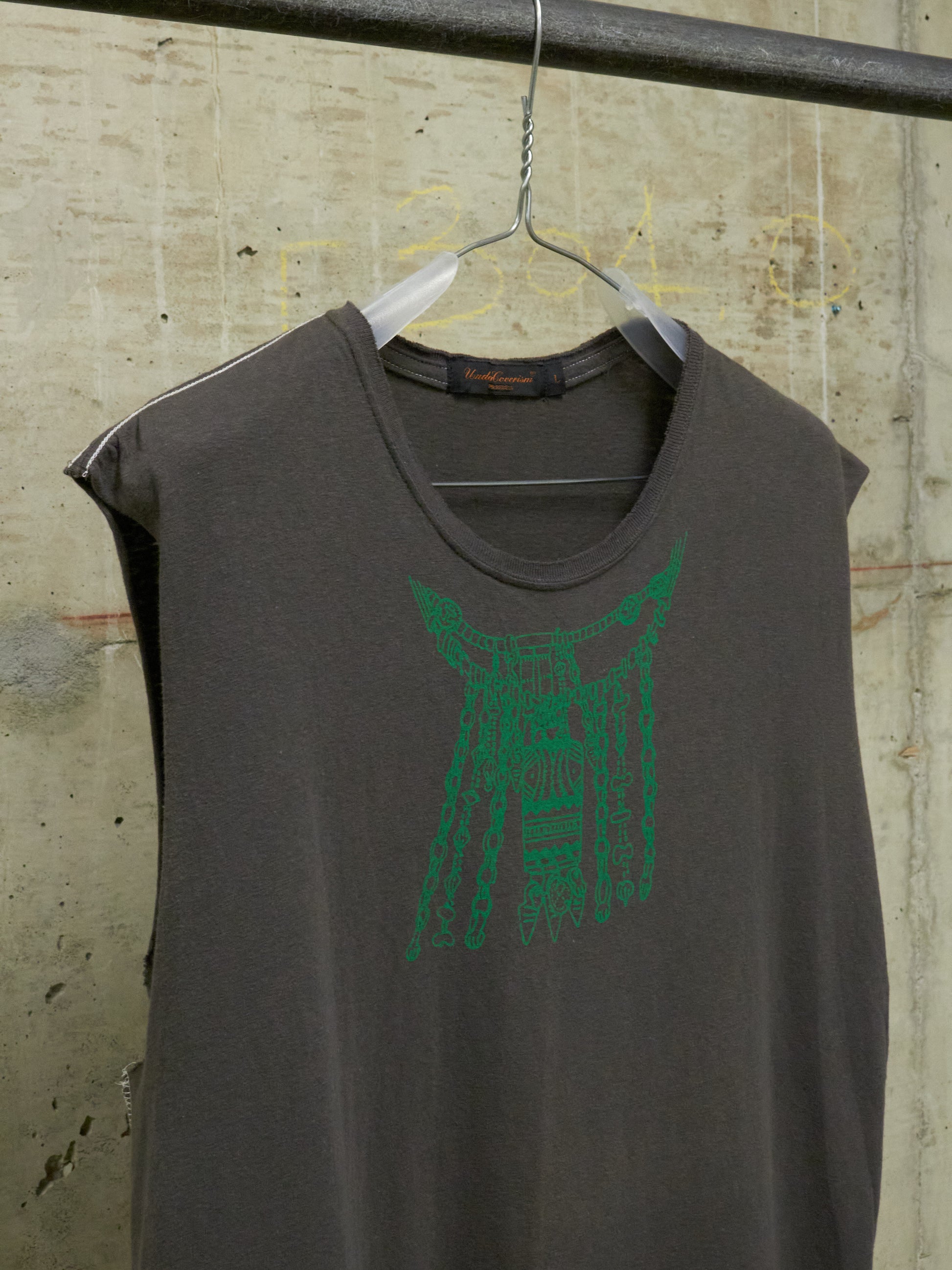 Gray sleeveless shirt with green graphic on a hanger against a textured wall.