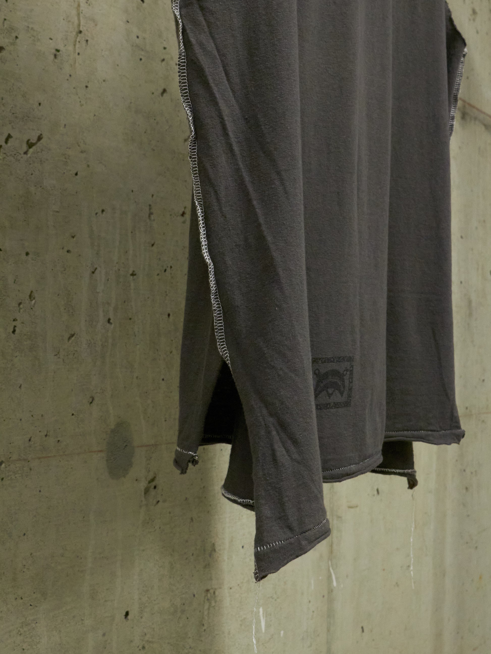 Gray sleeveless shirt with a brand logo hanging against a concrete wall.