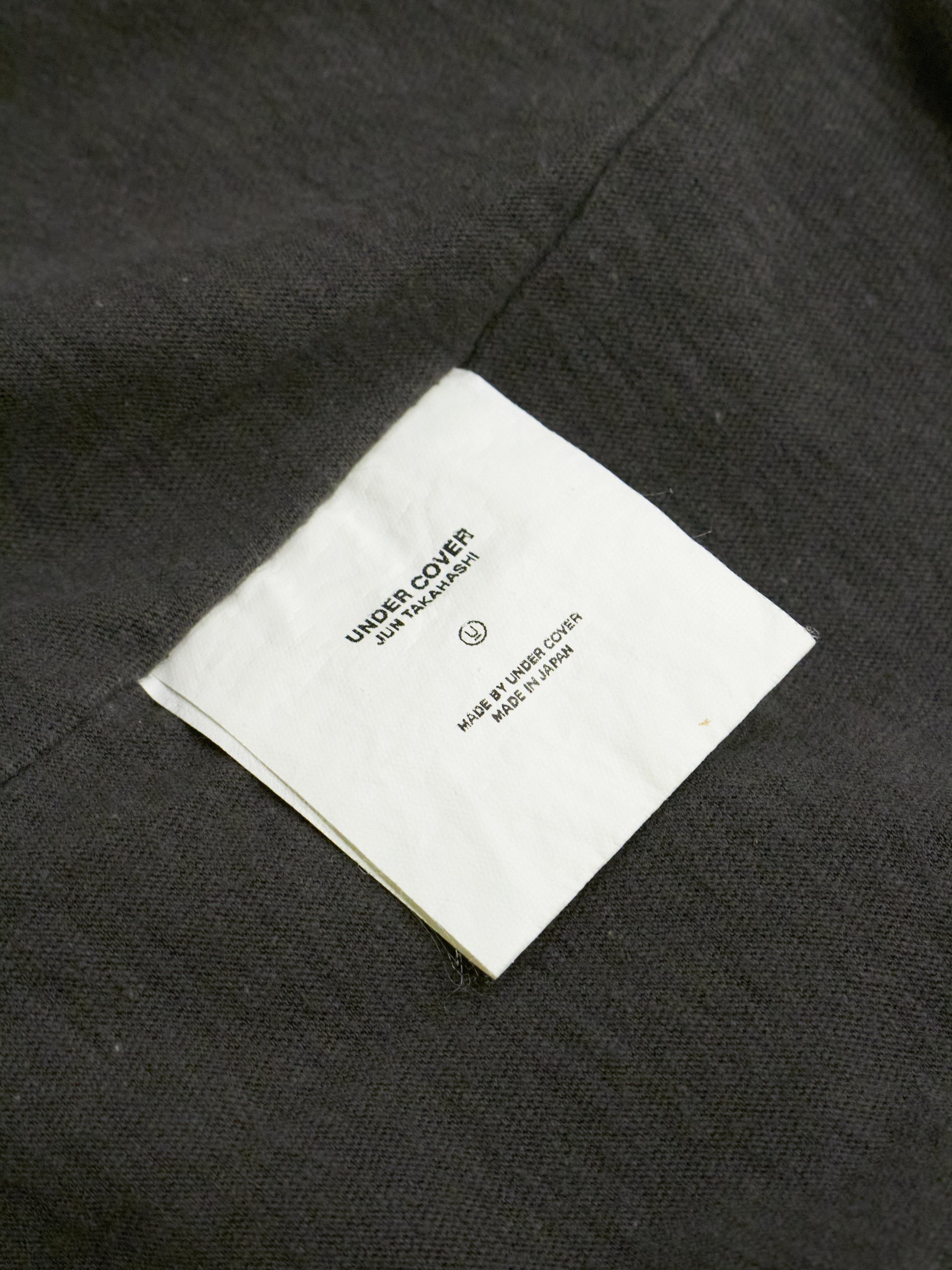 Close-up of a label on a dark fabric surface with 'Undercover' branding.