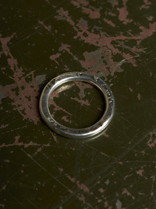 A silver metal ring with engraved markings, resting on a dark, distressed surface with peeling reddish-brown paint.