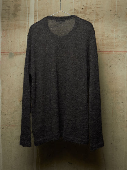 A dark charcoal gray knit sweater with a crew neck and long sleeves, hanging on a wire hanger against a textured concrete wall.