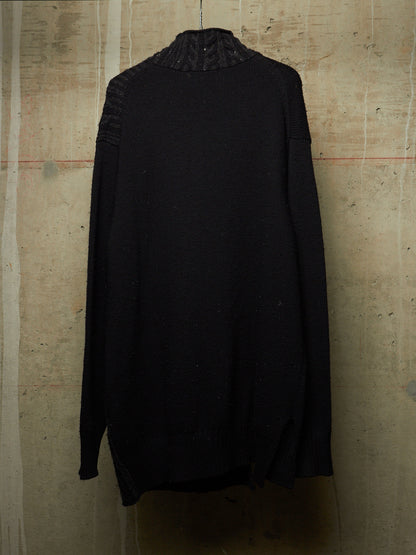 A black knit sweater with a textured, ribbed mock neck and ribbed sleeve cuffs, hanging against a textured concrete wall.