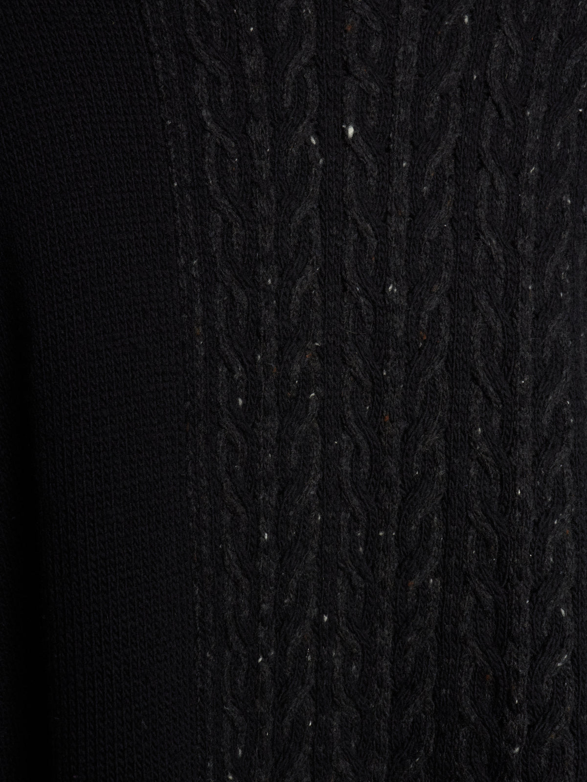 Close-up of a black knit sweater showing a textured cable-knit pattern on the right side and a smoother ribbed knit on the left side.