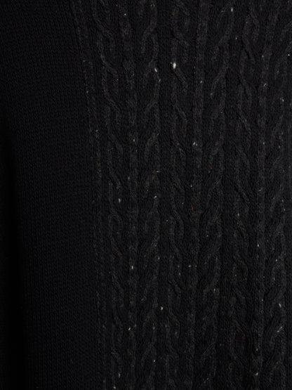 Close-up of a black knit sweater showing a textured cable-knit pattern on the right side and a smoother ribbed knit on the left side.