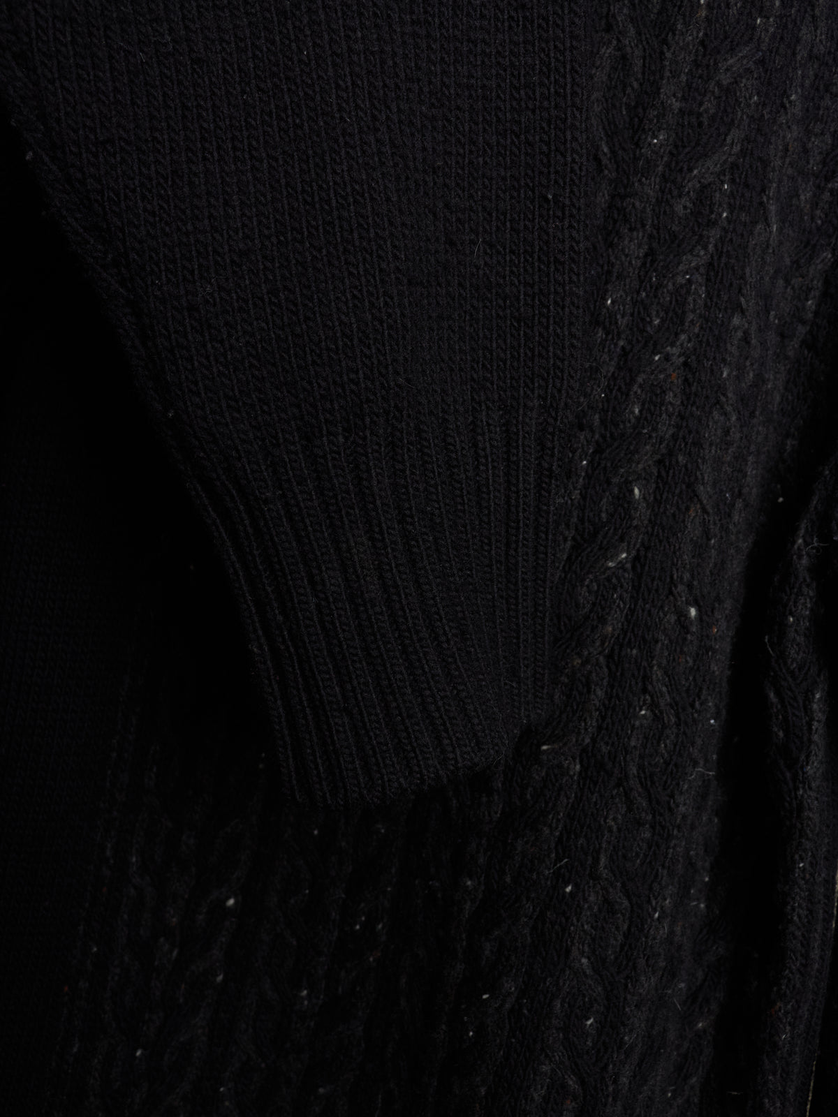 Close-up of a black knit sweater showing different textures including ribbed knit and cable knit patterns.