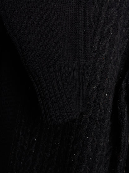 Close-up of a black knit sweater showing different textures including ribbed knit and cable knit patterns.