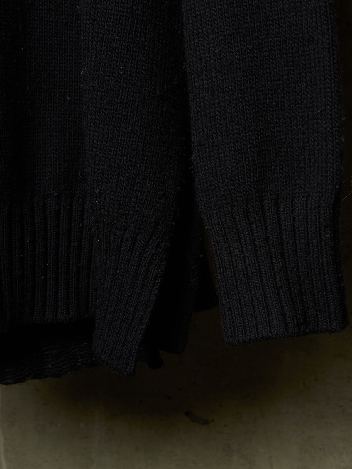 Close-up of a black ribbed knit garment, showing the texture and cuffs of a sweater or jacket against a dark background.