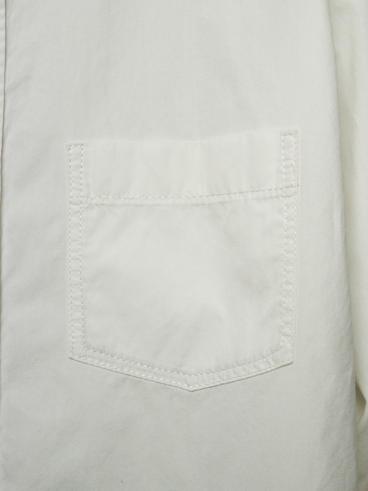 Close-up of a white fabric garment showing a single stitched chest pocket with visible texture and seam details.