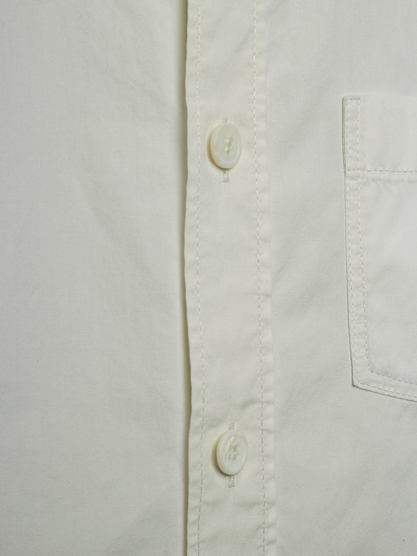 Close-up of a white button-down shirt showing the button placket, pocket seam, and fabric texture.