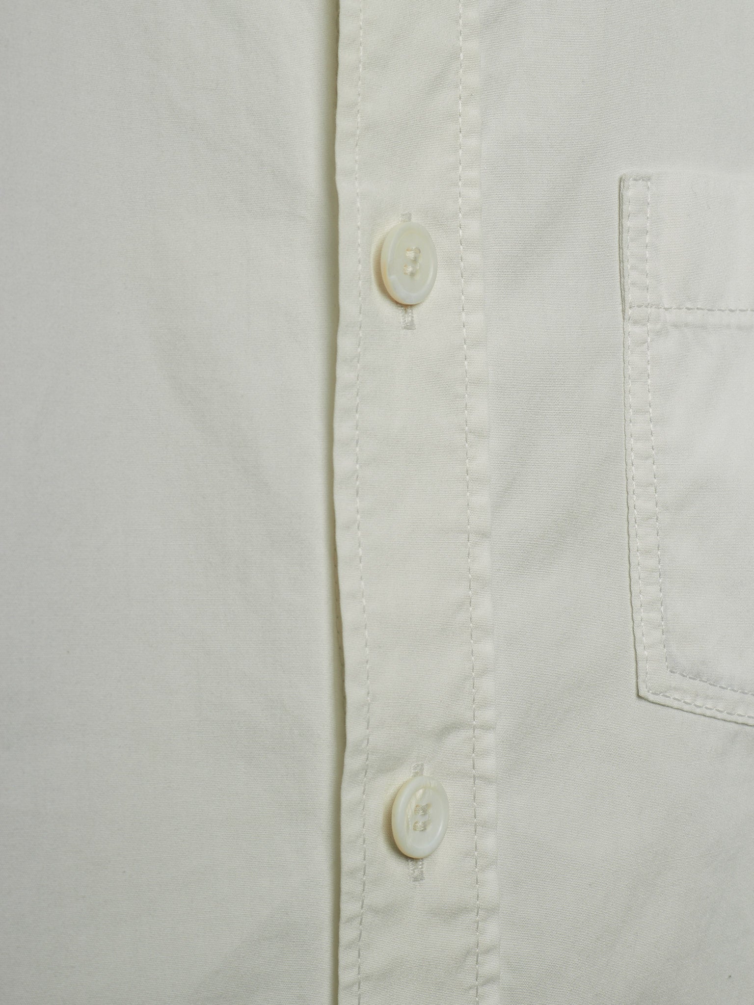 Close-up of a white button-down shirt showing the button placket, pocket seam, and fabric texture.